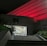 A hospital entrance is illuminated at night with red lighting that casts a dramatic glow on the building's facade. A flight of stairs leads up to the entrance, bordered by greenery, with a well-lit interior visible through the glass doors.