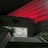 A hospital entrance is illuminated at night with red lighting that casts a dramatic glow on the building's facade. A flight of stairs leads up to the entrance, bordered by greenery, with a well-lit interior visible through the glass doors.